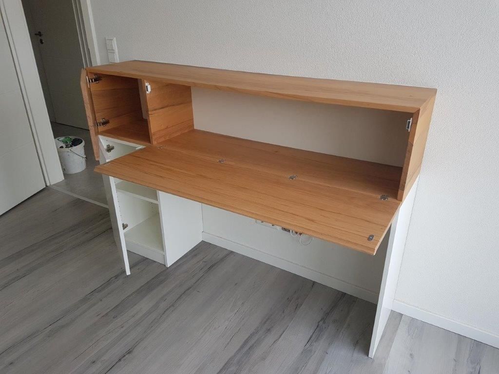 Ein Holzschreibtisch mit einem weißen Schrank darunter in einem Zimmer.