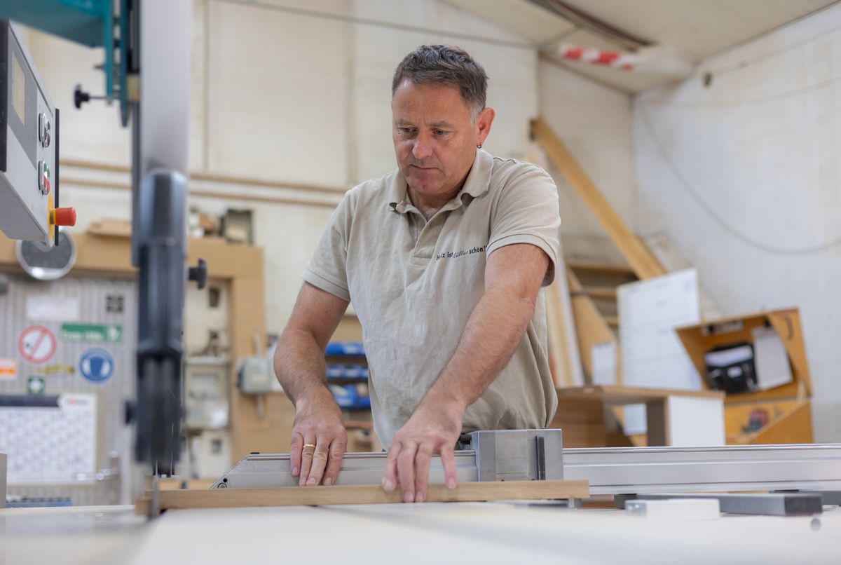 Ein Mann schneidet in einer Werkstatt mit einer Bandsäge ein Stück Holz.