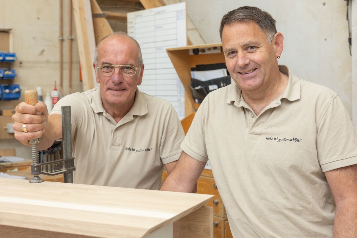 Zwei Männer bearbeiten in einer Werkstatt ein Stück Holz.