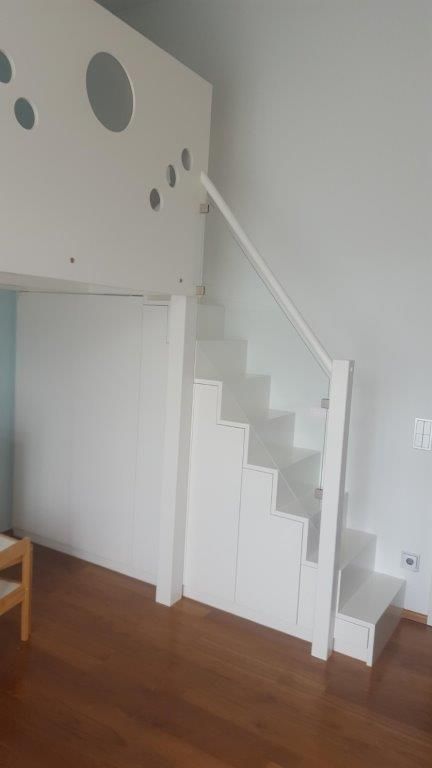 Eine weiße Treppe mit einem Glasgeländer in einem Wohnzimmer.