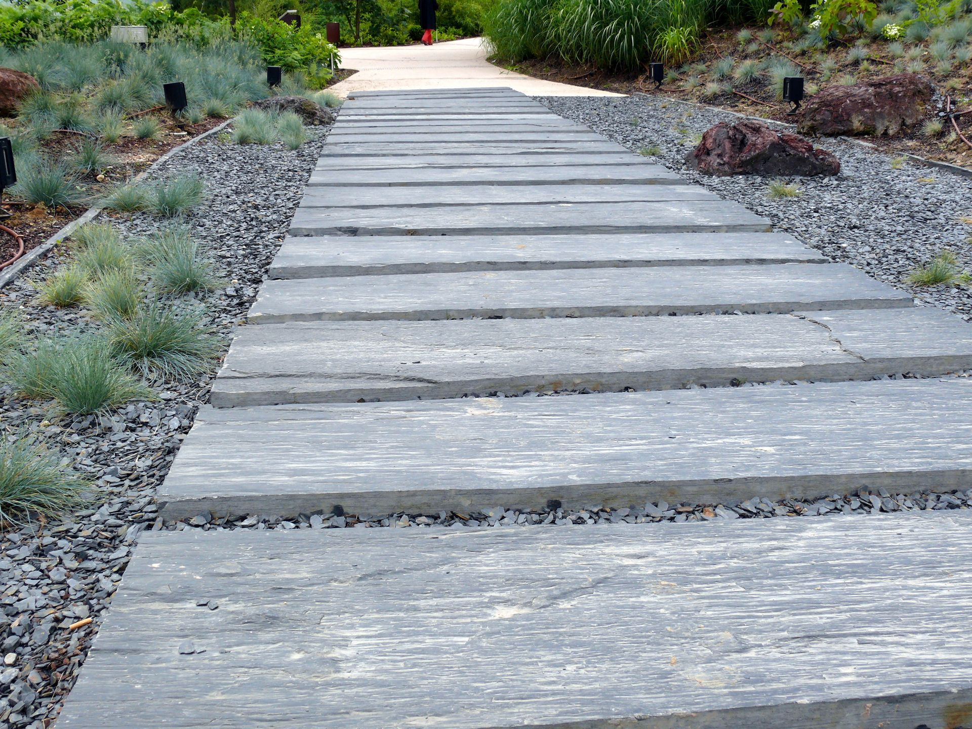 Chemin de pierres traversant un jardin, bordé de gravier et de plantes.