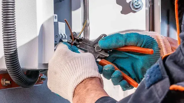 Un hombre está trabajando en una caja eléctrica con alicates.