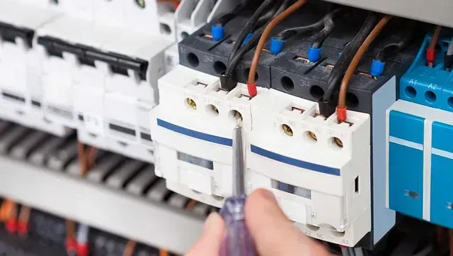 Una persona está trabajando en una caja eléctrica con un destornillador.