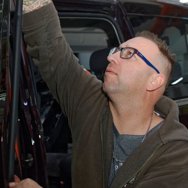 Ein Mann mit Brille streckt die Hand aus, um eine Autotür zu öffnen