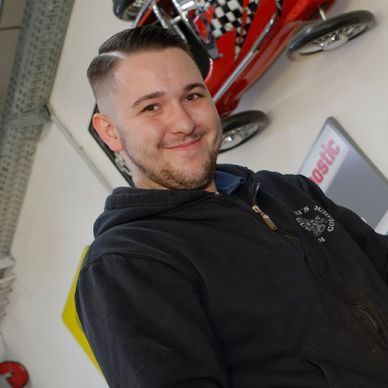 Ein Mann in einem schwarzen Kapuzenpullover lächelt vor einem Schild