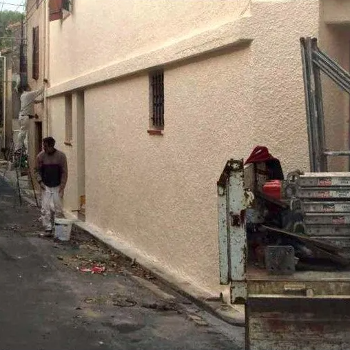 Deux hommes effectuent un ravalement de façade avec du crépi sur une maison