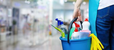 Mit gelben Handschuhen wird ein Fenster mit einem blauen Tuch und einer Sprühflasche gereinigt.