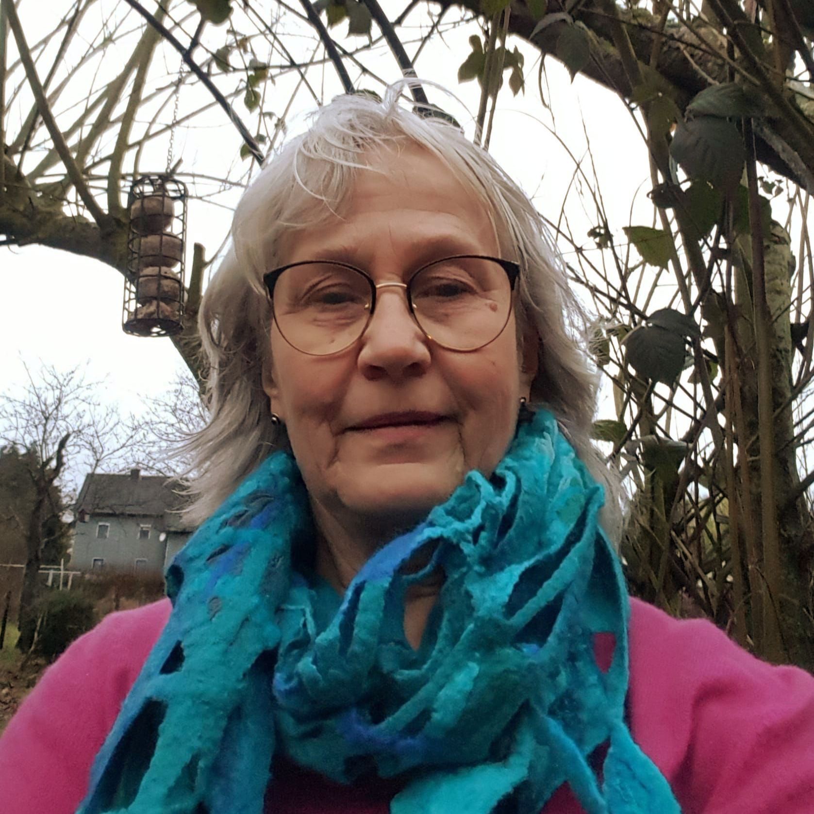 Eine Frau mit einem lila Schal steht vor einem Busch.