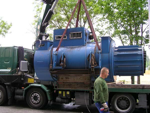 Homme devant un camion qui transporte une machine bleue