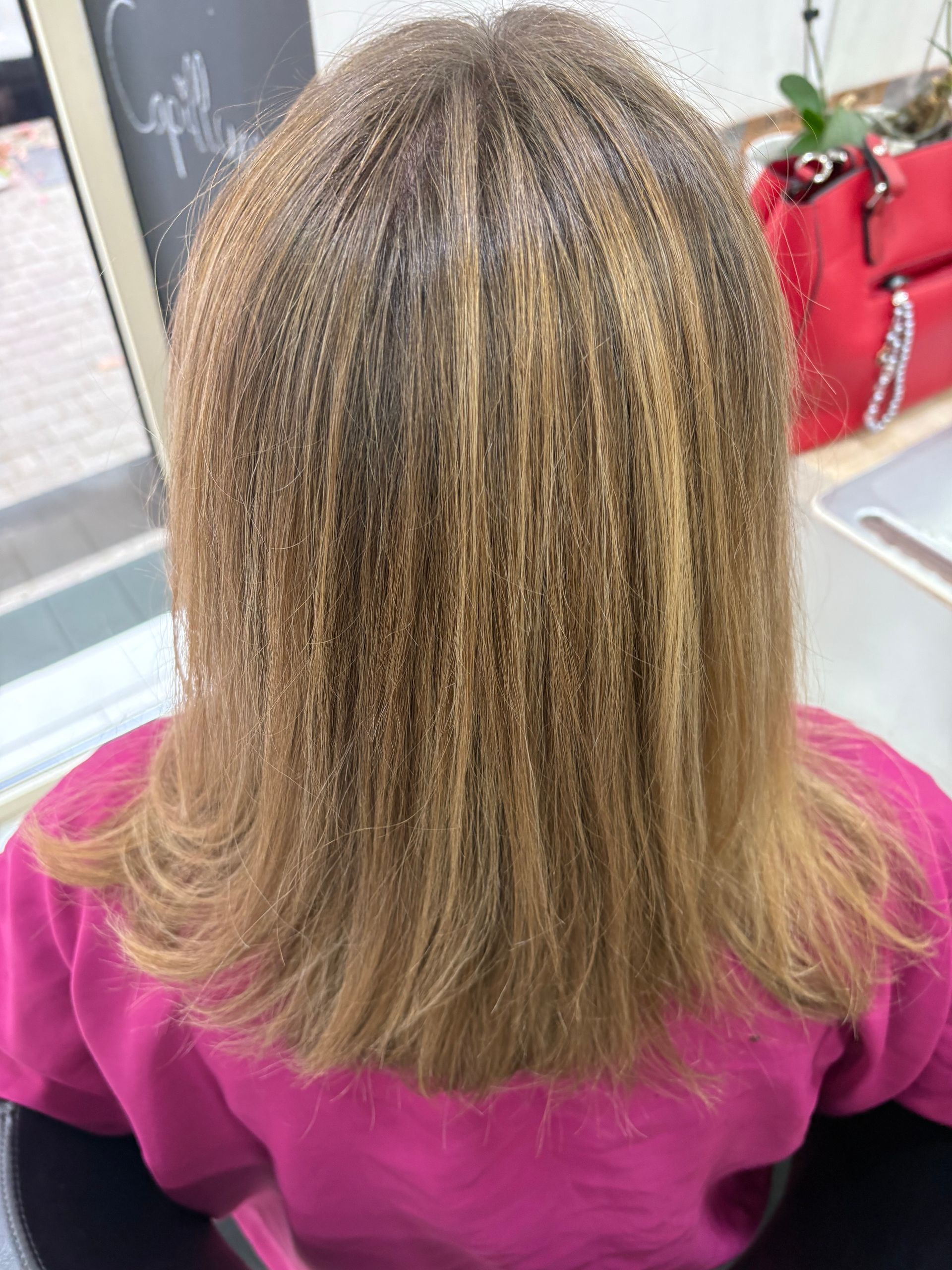 Femme aux cheveux blond-brun ondulés, portant une chemise rose, vue de dos.