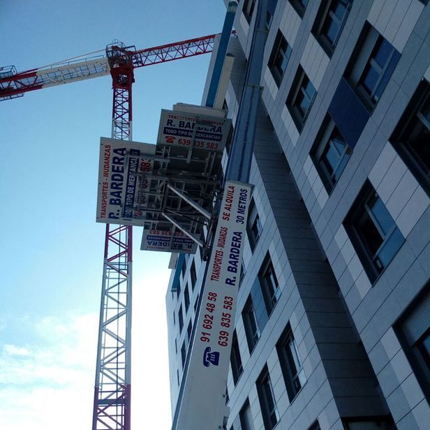 Una grúa eleva una plataforma junto a un edificio de varios pisos. La plataforma lleva el nombre de la empresa