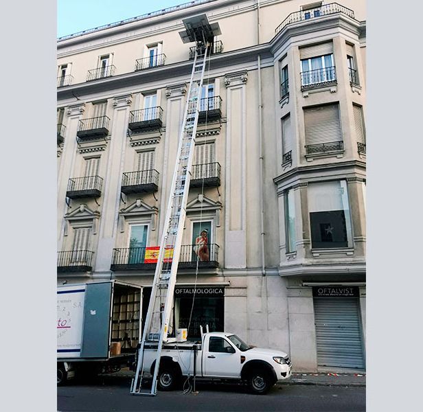 Un camión de mudanzas con una escalera alta está apoyado contra un edificio de apartamentos.