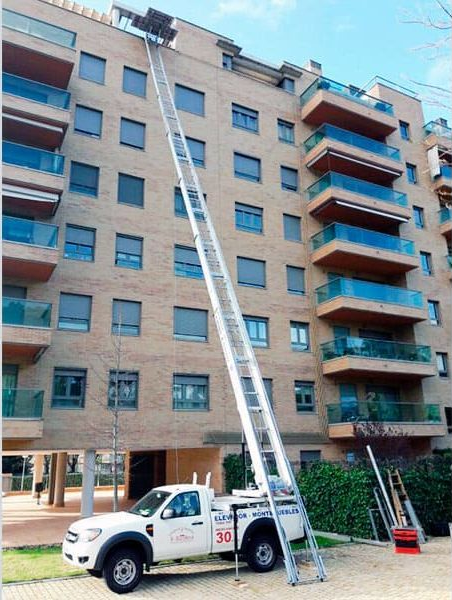 Un camión blanco con un elevador extendido al lado de un edificio.