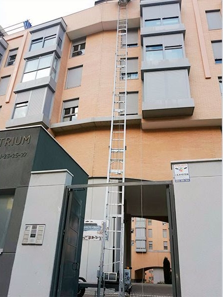 Una escalera alta se extendía por el costado de un edificio de ladrillo de varios pisos, a través de una puerta abierta.