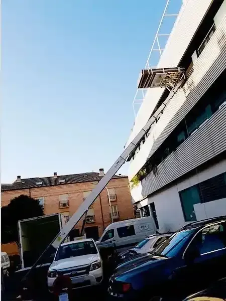 Un montacargas se extiende hasta un edificio con plataforma. Hay varios coches aparcados cerca. Cielo azul.