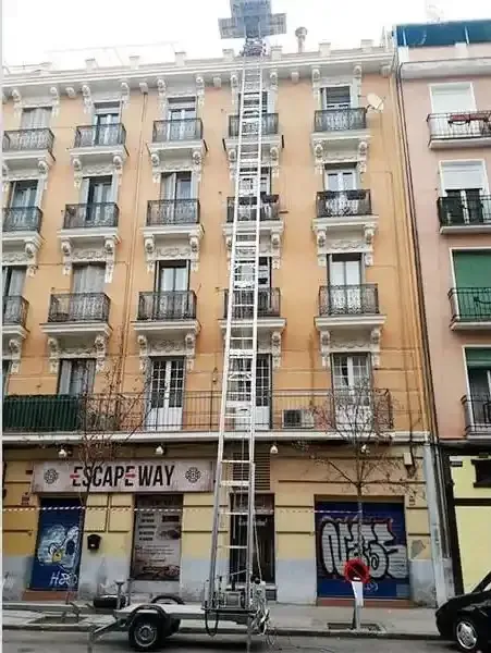 Un alto ascensor de aluminio se extiende hasta un edificio de apartamentos de color beige.