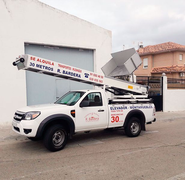 Camión blanco con plataforma de 30 metros. Está estacionado frente a un edificio; parece ser una empresa de mudanzas.
