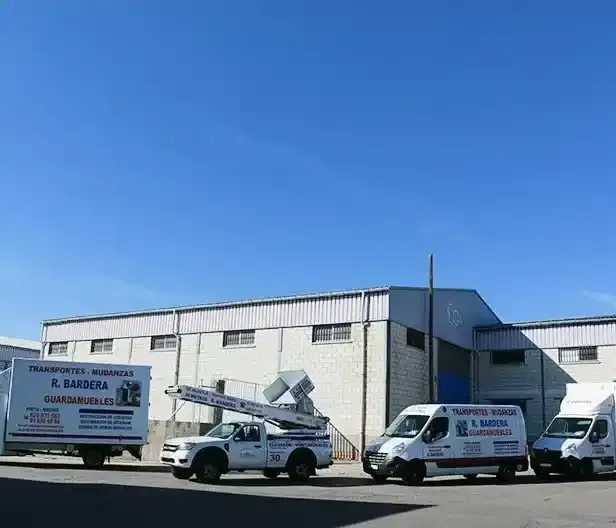 Camiones estacionados frente a un edificio industrial blanco bajo un cielo azul, anunciando servicios de mudanzas.
