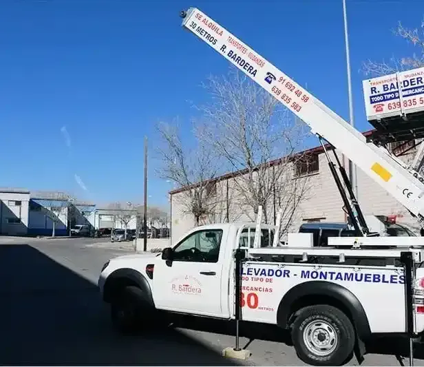 Camión con elevador incorporado, usado para mover muebles. Cielo azul, camión blanco, entorno industrial.