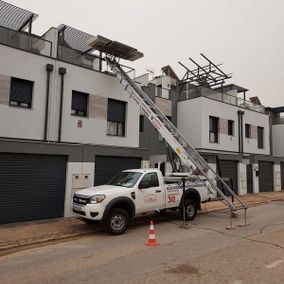 Camión blanco con elevador al lado de un edificio, cono de tráfico naranja.