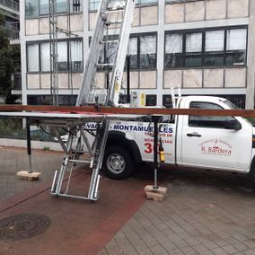 Camión con plataforma elevadora situado junto a un edificio, posiblemente para mover muebles.
