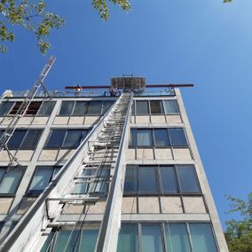 El elevador de un camión de mudanzas llega al techo de un edificio de gran altura bajo un cielo azul y traslada artículos.