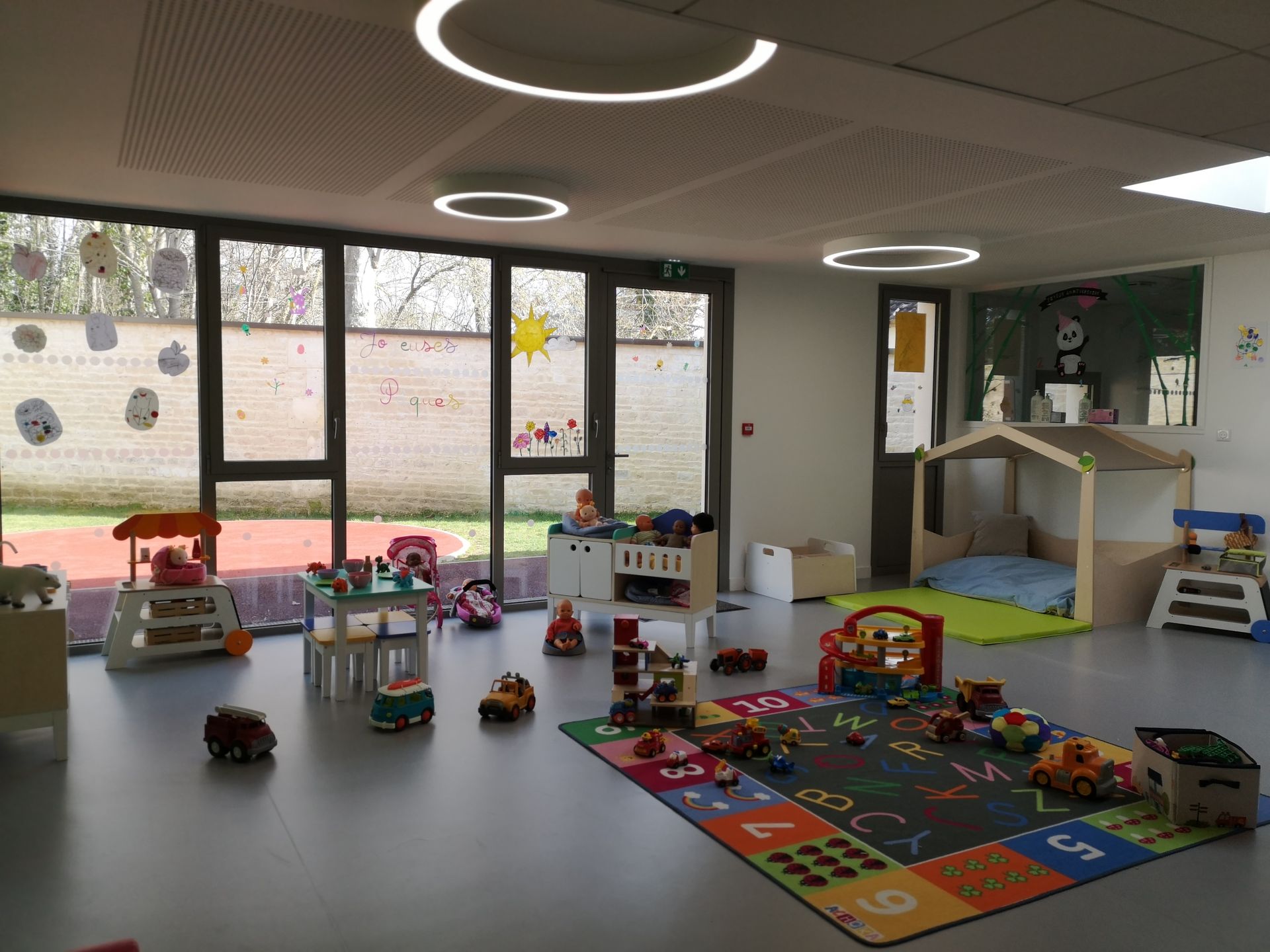 Salle de jeux avec des jouets éparpillés sur le sol, un tapis éveil et des étagères.