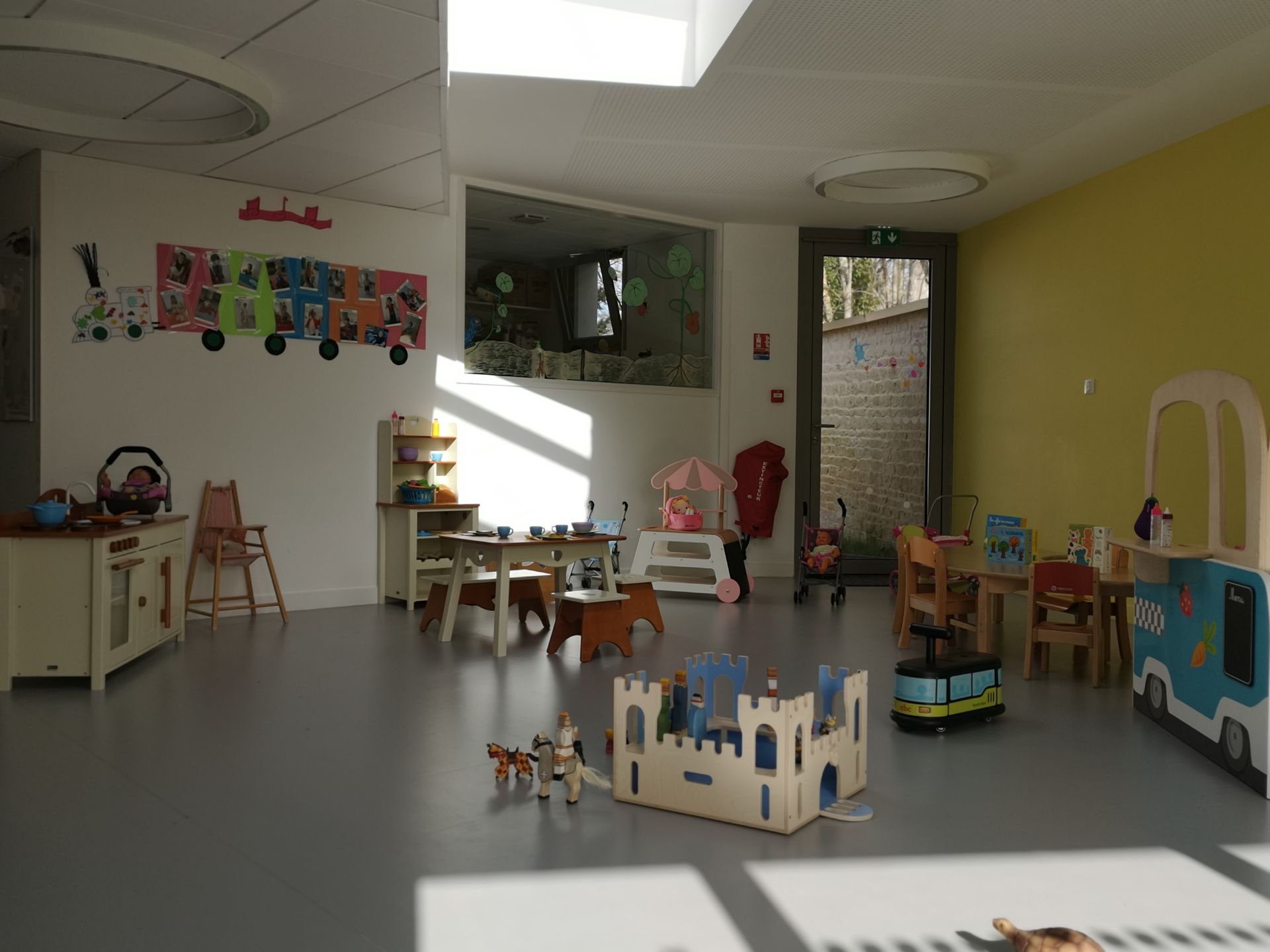 Salle de jeux avec des jouets, dont un château en bois, une table, des chaises et un train miniature.