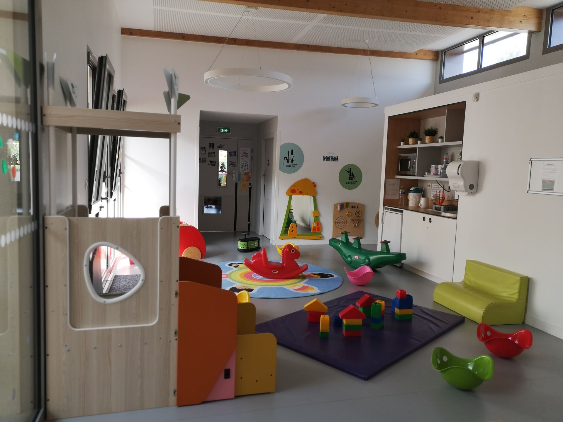 Salle de jeux avec jouets, sièges confortables et structure de jeux en bois. Couleurs claires et neutres.