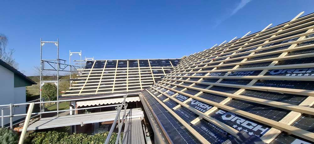 Auf einem Haus wird ein Dach gebaut, im Hintergrund ist ein blauer Himmel zu sehen.