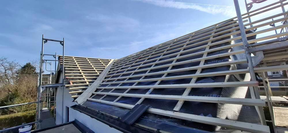 Auf einem Haus wird ein Dach gebaut, im Hintergrund ist ein blauer Himmel zu sehen.