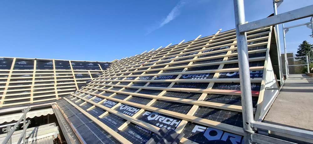 Ein Dach wird gebaut, im Hintergrund ein Gerüst, blauer Himmel.