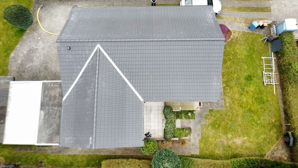 Eine Luftaufnahme eines Hauses mit grauem Dach und einem davor geparkten weißen Auto.