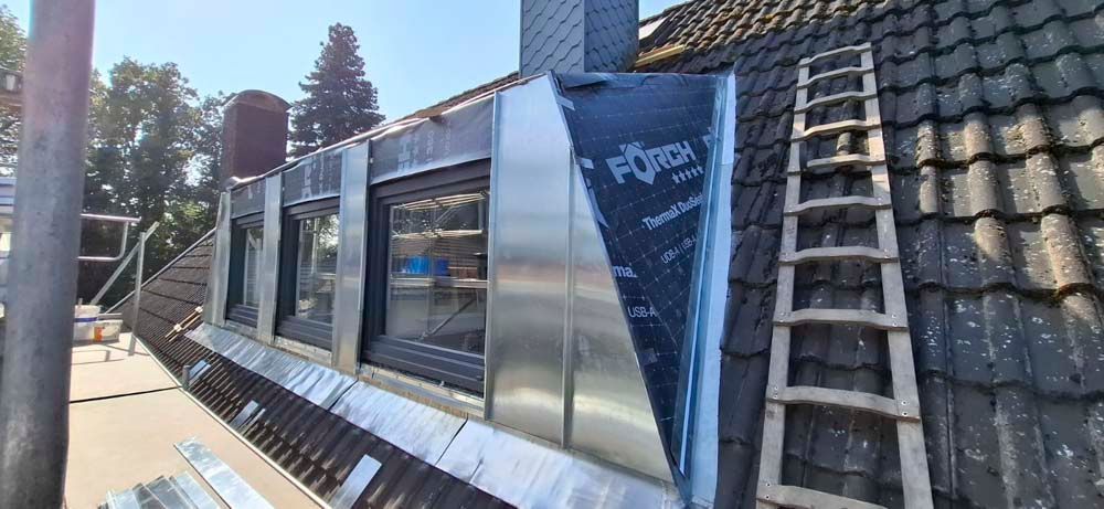 Auf einem Dach steht neben einem Fenster eine Leiter.