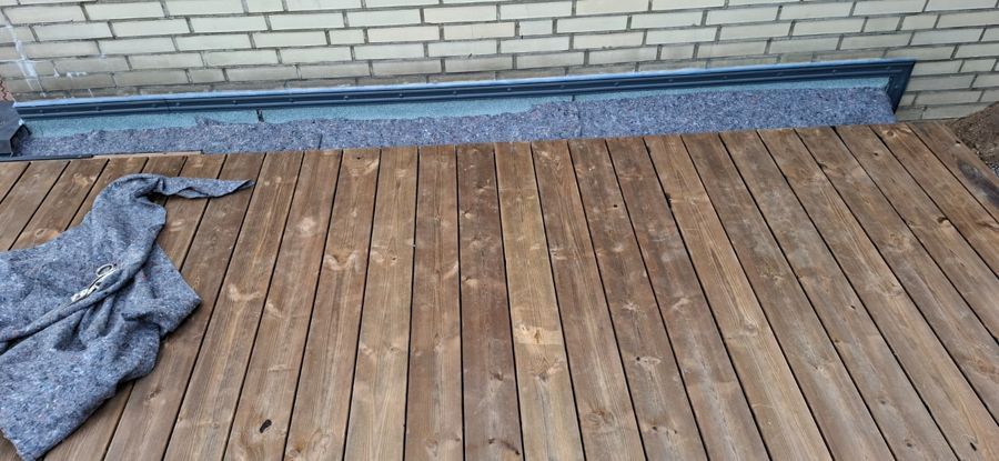 Ein Holzdeck mit einer Decke darauf vor einer Backsteinmauer.