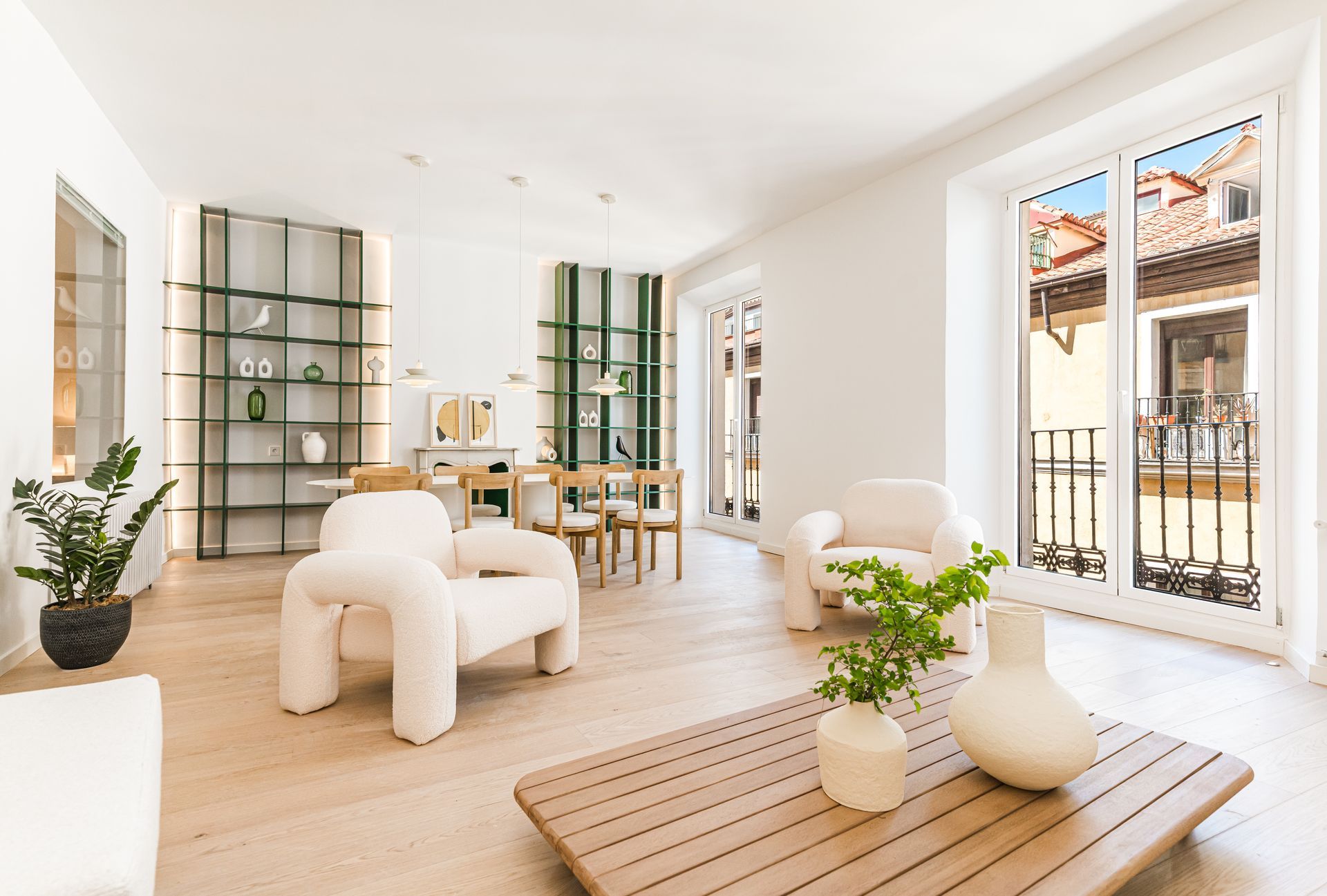 Sala de estar moderna y luminosa, de color blanco, con muebles de madera, plantas verdes y grandes ventanales con rejas de hierro.