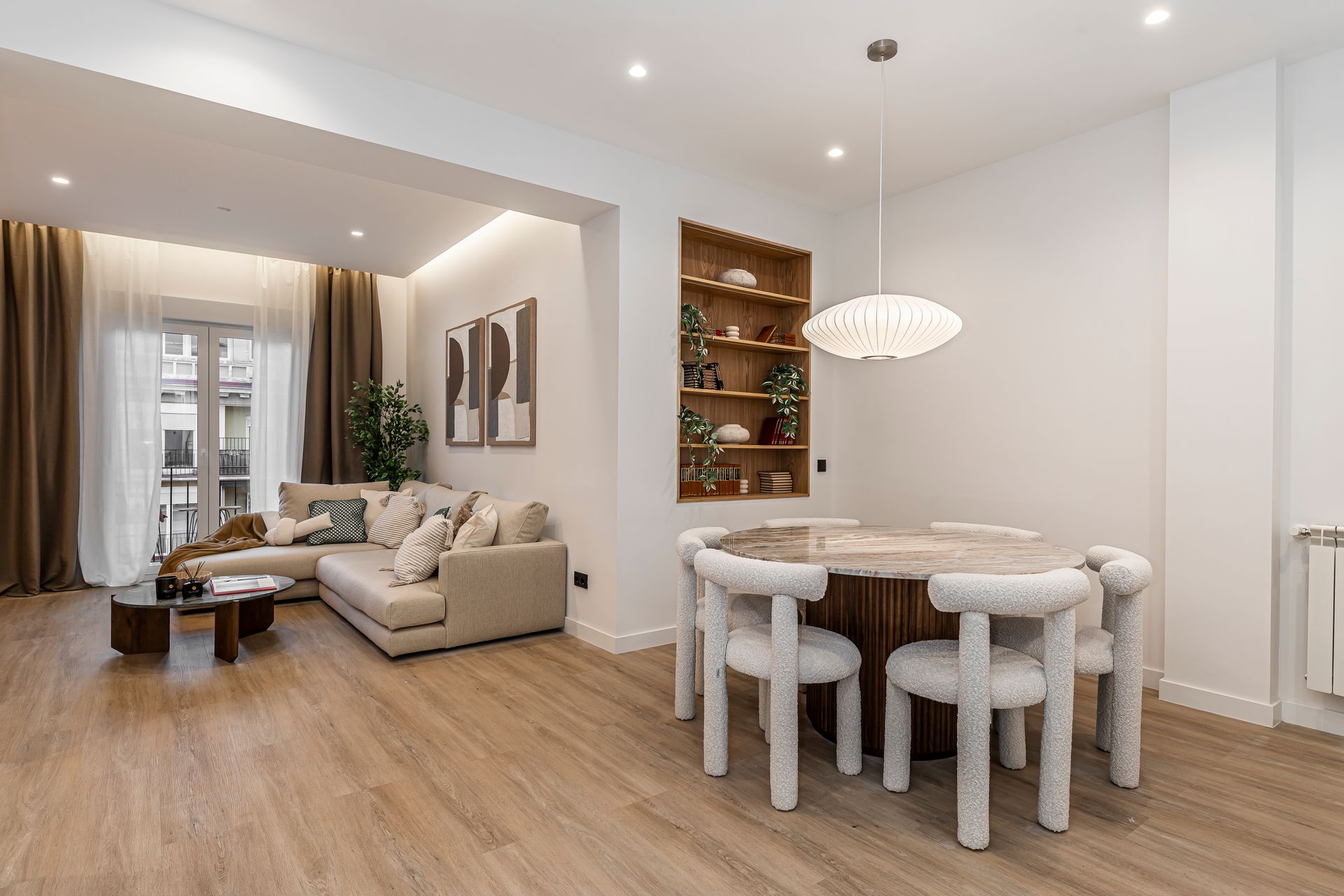 Salón-comedor moderno de planta abierta con sofá beige, mesa de comedor redonda y suelo de madera.