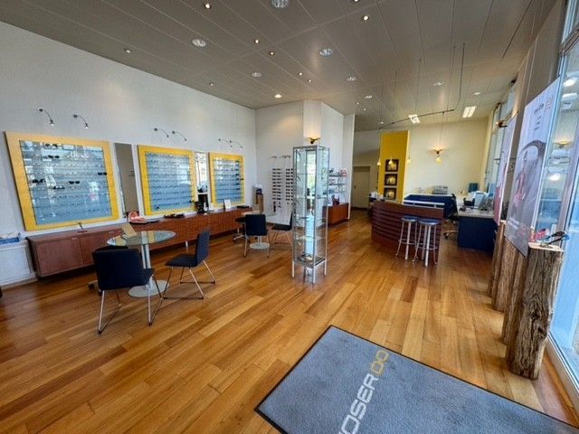 Innenansicht eines Optikergeschäfts mit Brillenauslagen, Tischen und Holzboden.