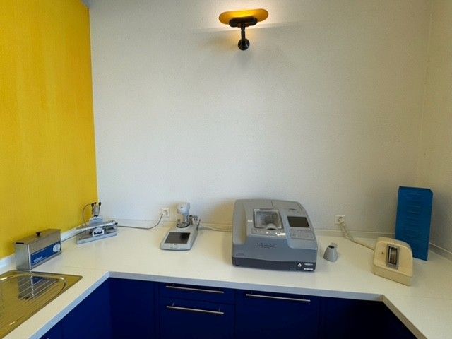 Ein hellgelber und weißer Arbeitsbereich mit medizinischen Geräten, blauen Schränken und einer gelben Wand.