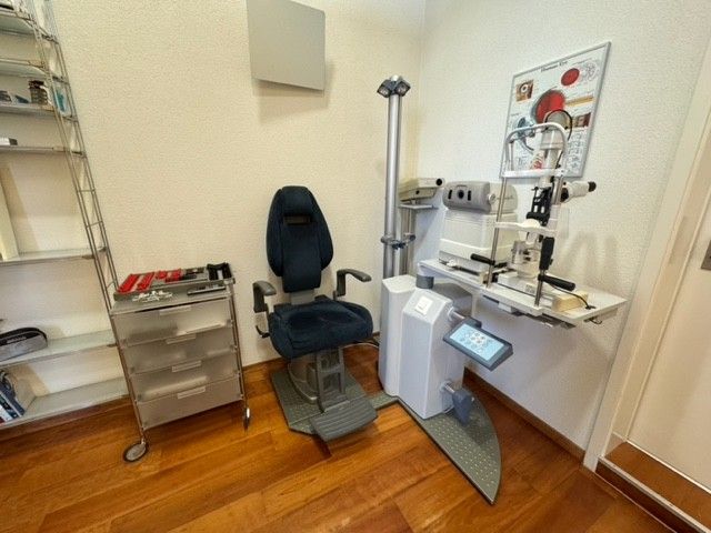 Augenuntersuchungsraum mit Stuhl, medizinischen Geräten und Sehtafel.