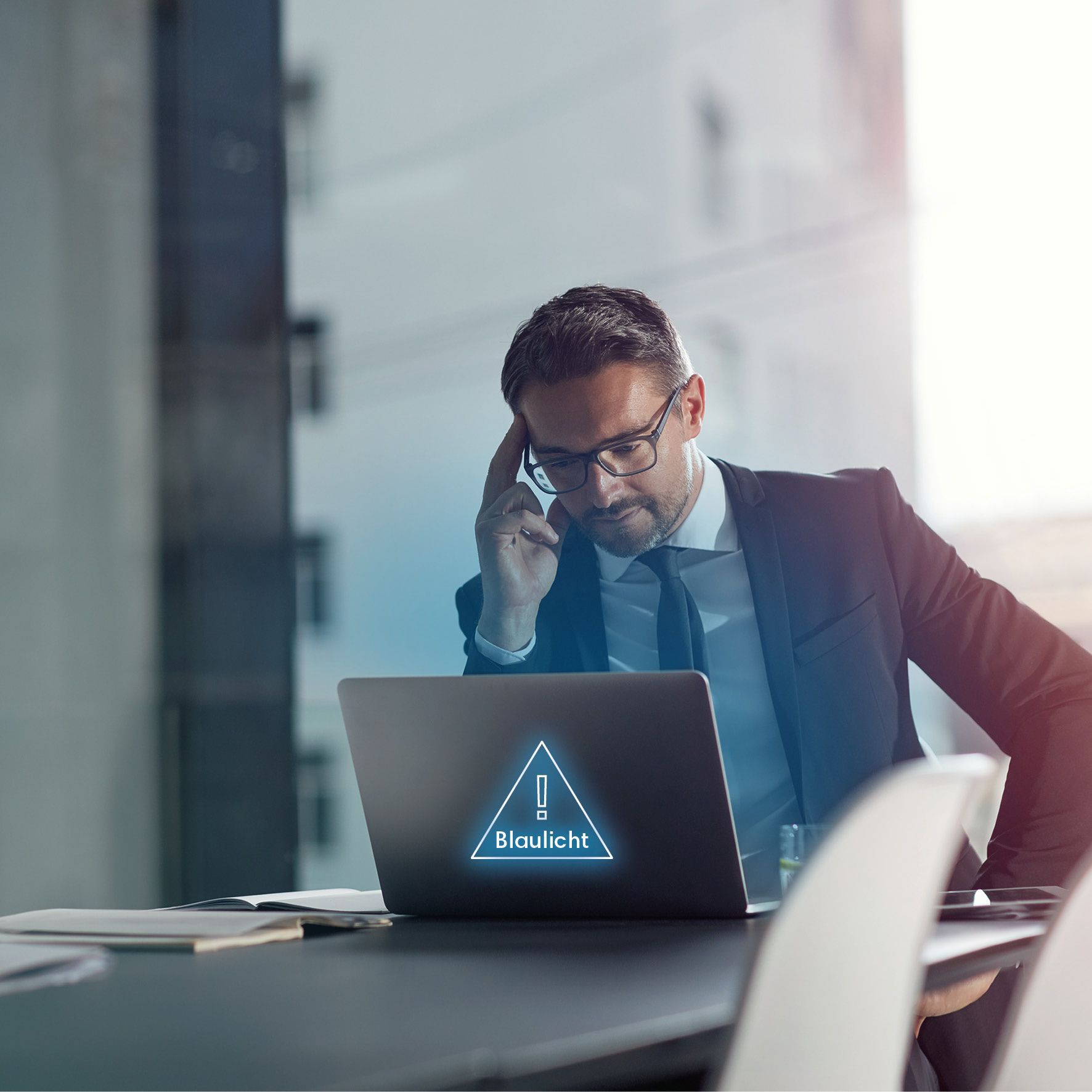 Ein Mann im Anzug sitzt gestresst vor seinem Laptop, auf dessen Bildschirm eine Warnmeldung erscheint.