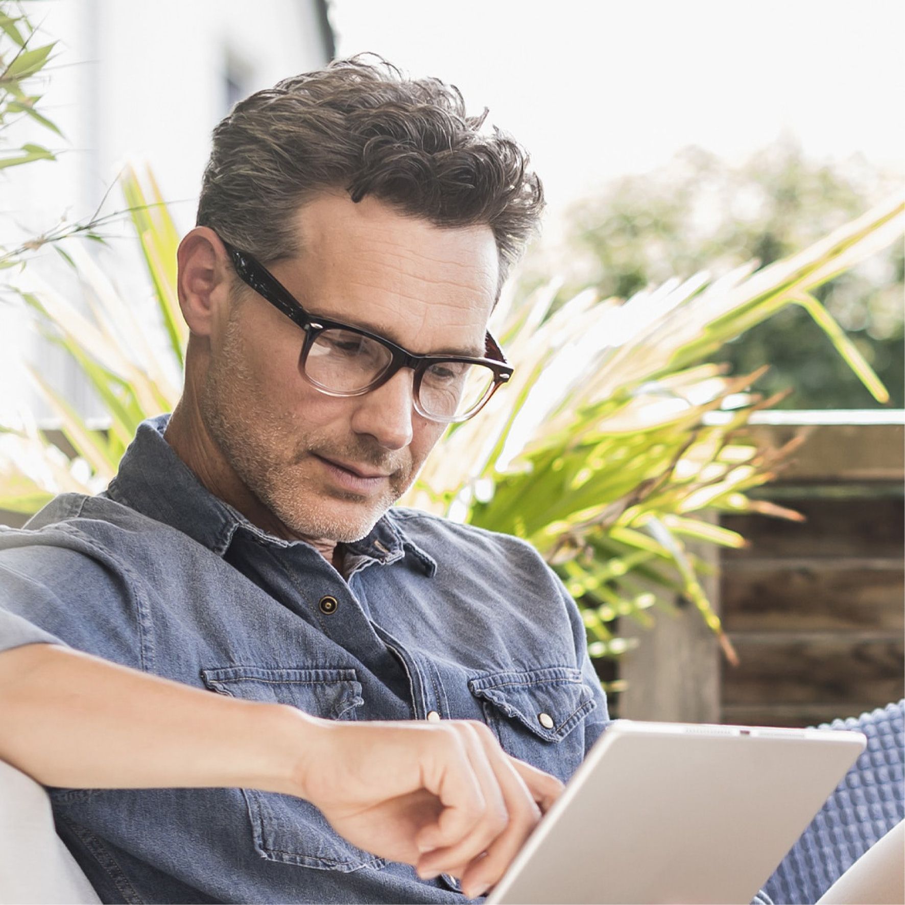 Mann mit Brille, der im Freien ein Tablet benutzt, konzentrierter Gesichtsausdruck.