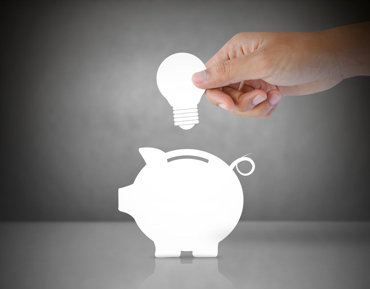 Mano colocando una bombilla en una alcancía.