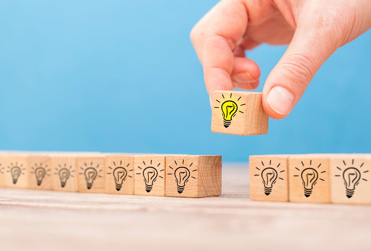 Mano colocando un bloque de bombilla sobre una línea de bloques de bombilla, sobre una superficie de madera contra un fondo azul.