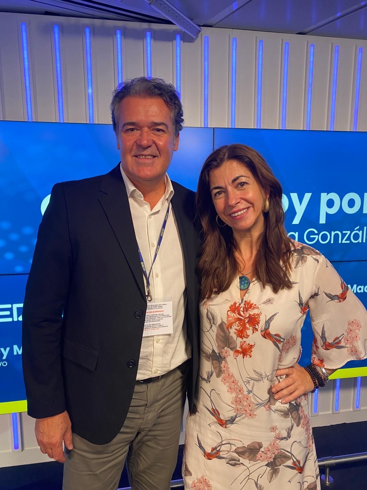 Un hombre y una mujer posan para una fotografía frente a una pantalla grande.