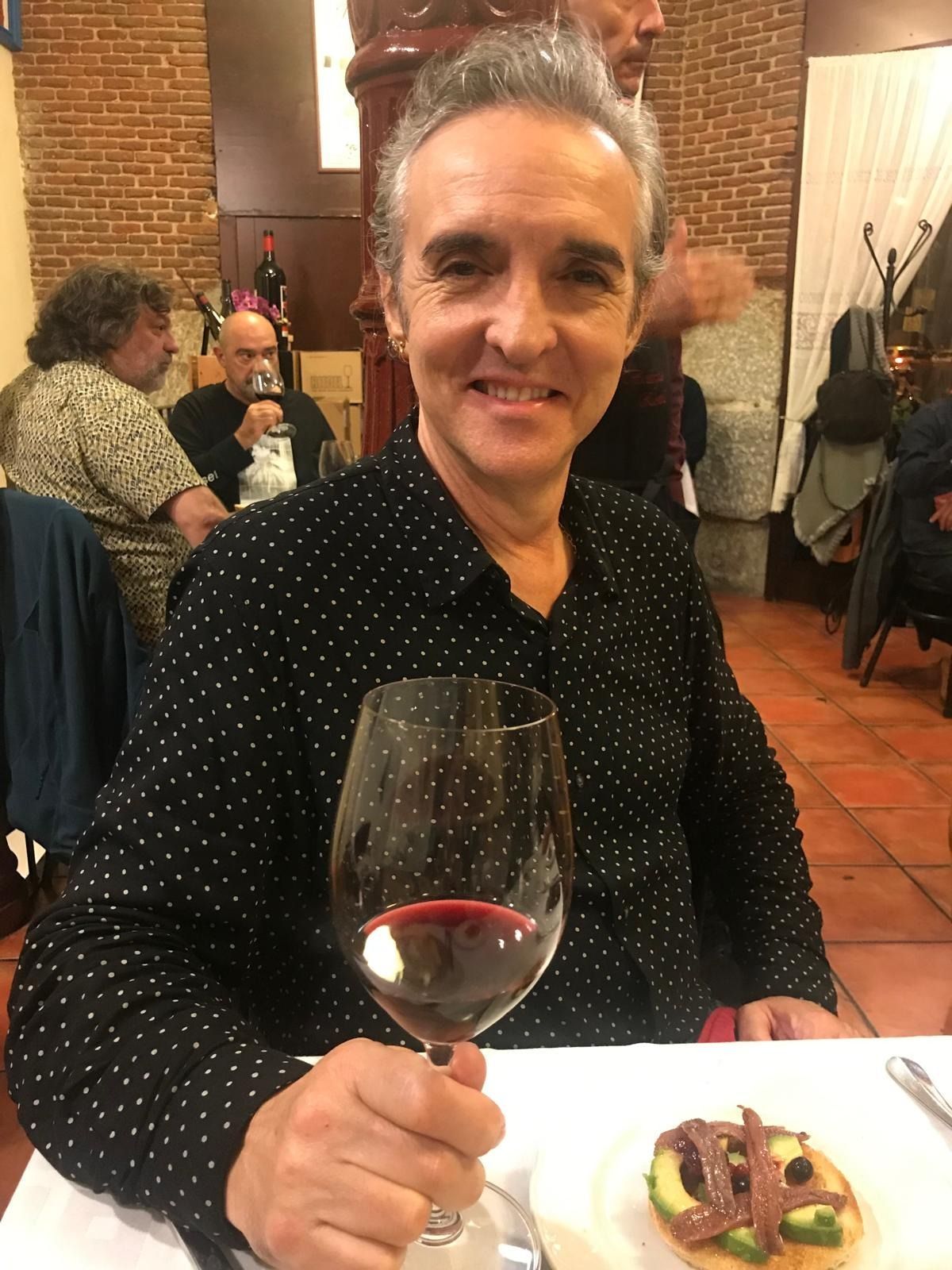 Un hombre está sentado en una mesa sosteniendo una copa de vino.