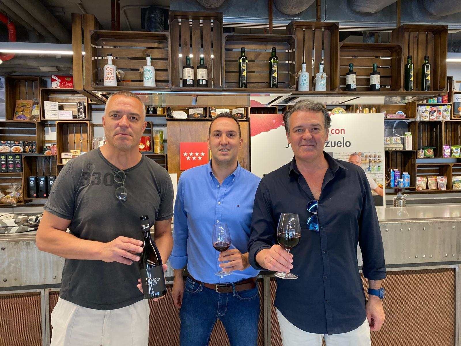 Tres hombres están de pie uno al lado del otro sosteniendo copas de vino y botellas de vino.