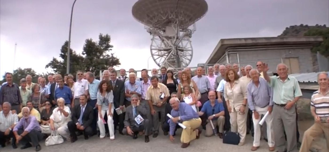 Un grupo grande de personas posa para una foto frente a una gran antena parabólica.