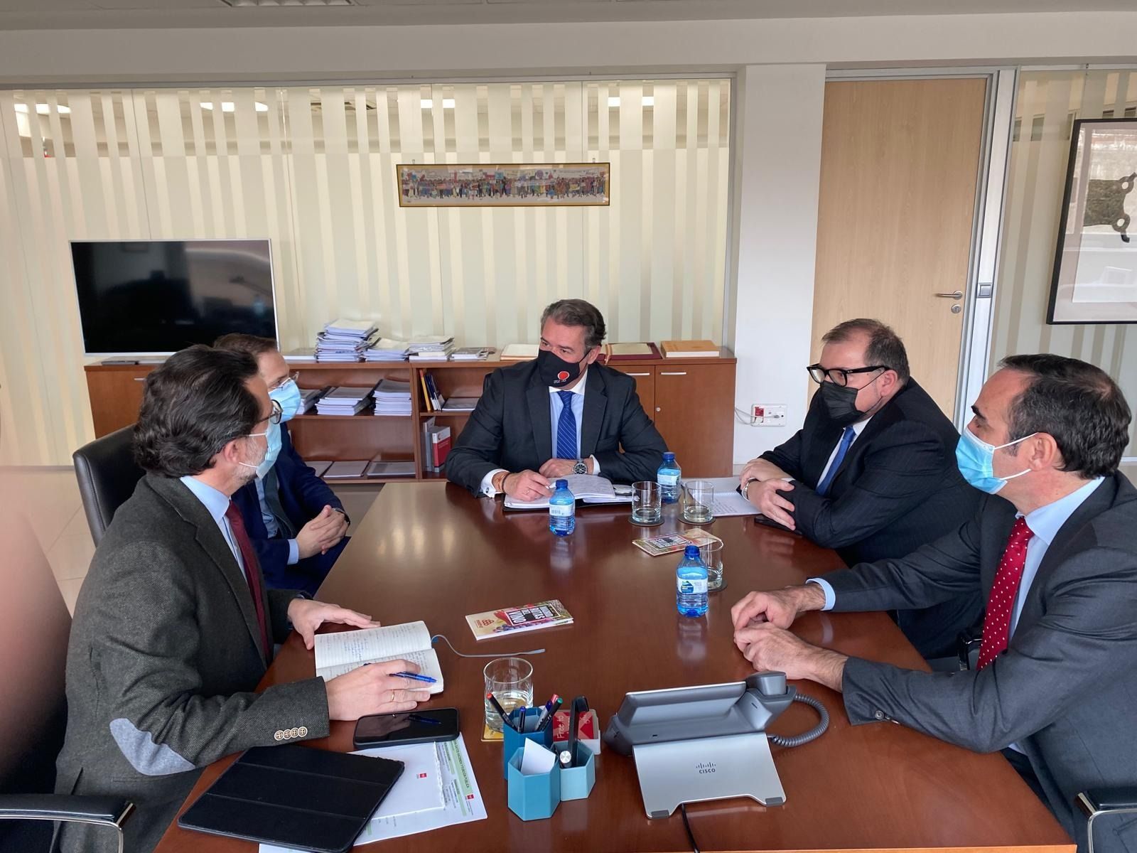 Un grupo de hombres están sentados alrededor de una mesa usando máscaras faciales.