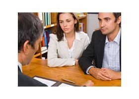 Dos personas vestidas de traje escuchan atentamente al otro lado de una mesa durante una reunión.